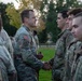 A U.S. Army officer or senior NCO is shaking hands with soldiers lined up in formation, likely during a recognition or greeting ceremony. All personnel are wearing Operational Camouflage Pattern (OCP) uniforms. The setting appears to be an outdoor grassy area, possibly on a military installation or ROTC campus.