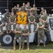 A group of U.S. Marines from MALS-31 'Stingers' pose for a unit photo on and around a white TLD aircraft ground support tug vehicle. The personnel are wearing olive drab t-shirts and MARPAT camouflage trousers, arranged in multiple rows. A yellow and black 'Stingers MALS-31' unit insignia sign is prominently displayed in the center of the group.
