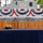A ceremonial display table covered in a blue cloth holds multiple engraved wooden boxes/cases arranged in a row, with a Navy chief petty officer's combination cover (hat) placed in front of them. The boxes appear to be personalized chief petty officer initiation or advancement ceremony cases, each bearing individual names, ratings, and a date of September 16th, 2026, Class 133. The setting is decorated with patriotic red, white, and blue bunting, with a naval vessel visible in the background.