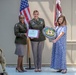 Three individuals pose for a formal recognition ceremony at Blanchfield Army Community Hospital. Two are wearing U.S. Army dress uniforms while a third civilian woman stands alongside them. The group is holding a certificate and a Blanchfield Army Community Hospital commemorative plaque.