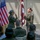 Two female U.S. Army officers are conducting what appears to be a military oath or promotion ceremony, both with right hands raised. They are standing before an American flag and a maroon U.S. Army Medical Corps unit guidon, with an audience of uniformed and civilian personnel seated in the foreground. The setting appears to be an indoor or covered outdoor military facility.