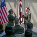 Two female U.S. Army officers are conducting what appears to be a military oath or promotion ceremony, both with right hands raised. They are standing before an American flag and a maroon U.S. Army Medical Corps unit guidon, with an audience of uniformed and civilian personnel seated in the foreground. The setting appears to be an indoor or covered outdoor military facility.
