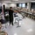 A civilian instructor in black clothing is conducting a training briefing for a large group of military personnel in Army combat uniforms (ACU/OCP pattern). The session appears to be a medical or tactical training class, with medical supplies and equipment visible on a table in the foreground. The soldiers are seated at long tables arranged in a U-shape configuration within a modern classroom facility.