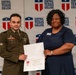 A military service member in Army dress uniform and a civilian woman in a navy dress are jointly holding a Certificate of Completion from Central Texas College. The ceremony appears to be an academic achievement recognition event held in front of a Central Texas College branded backdrop. The certificate visible in the image appears to be made out to 'Anthony Balin', which also matches the name tag on the soldier's uniform.
