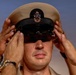 A U.S. Navy Chief Petty Officer is having his combination cover (cap) placed on his head, likely during a promotion or pinning ceremony. Two sets of hands are visible adjusting the khaki cover, which bears the USN anchor insignia. This appears to be a formal military advancement ritual.