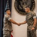 Two U.S. Marine Corps personnel in MARPAT digital camouflage uniforms are shaking hands in front of an official backdrop featuring the Great Seal of the United States of America. The setting appears to be a formal military ceremony, likely a promotion, award, or recognition event. The flags of the United States and Panama are visible in the background, suggesting this event took place at a U.S. diplomatic or military facility in Panama.