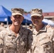 Two U.S. Marines in desert MARPAT camouflage uniforms pose together smiling at what appears to be an outdoor military event or gathering. The Marine on the left has a name tape reading 'LONG' and the one on the right appears to have a name tape reading 'BBANG' or similar. Both wear the Eagle, Globe, and Anchor emblem on their covers and chest insignia.