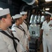 A senior U.S. Navy officer in dress white uniform is addressing three junior enlisted sailors (also in dress whites with Dixie cup covers) aboard what appears to be the bridge or interior passageway of a naval vessel. The officer displays multiple service ribbons and warfare insignia, indicating significant experience and rank. The setting appears to be an official visit, briefing, or orientation aboard a Littoral Combat Ship (LCS), as suggested by the name tags visible on the sailors' uniforms.
