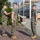 Chief Warrant Officer 2 Joshua J. Krantz’s Promotion Ceremony Three U.S. Marines in MARPAT woodland camouflage uniforms are gathered on a brick plaza in an outdoor military installation setting. One Marine on the left appears to be pinning an insignia or award onto the center Marine's uniform collar or chest area, suggesting a promotion or award ceremony. A third Marine stands at attention facing them, likely serving as a witness to the formal proceeding.