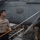 A U.S. Navy sailor is cleaning or washing an aircraft aboard the USS Abraham Lincoln aircraft carrier. The sailor is using a long-handled squeegee or brush tool to reach the aircraft's surface. The aircraft visible in the background is marked 'NAVY' and bears the designation 'EA-' with the number '1682', consistent with an EA-18G Growler or similar naval aircraft.
