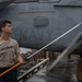 A U.S. Navy sailor is cleaning or washing an aircraft aboard the USS Abraham Lincoln aircraft carrier. The sailor is using a long-handled squeegee or brush tool to reach the aircraft's surface. The aircraft visible in the background is marked 'NAVY' and bears the designation 'EA-' with the number '1682', consistent with an EA-18G Growler or similar naval aircraft.