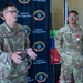 Two U.S. Air Force personnel are standing in front of an Andersen Fire Department backdrop, likely during a formal recognition ceremony. The airman on the right is wearing a red medal on his uniform, suggesting he is being honored or has recently received an award. The senior airman on the left appears to be speaking or presenting.