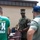 MCAS Beaufort Summer Bash A U.S. Marine in MARPAT camouflage uniform and cover is interacting with two civilians outdoors near a building. The Marine appears to be handling or moving a wooden/composite chair. One civilian is wearing a green St. Patrick's Day 5K Run/Walk event t-shirt.