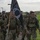 Team Andersen kick-off 24-hour POW/MIA memorial event A group of military personnel in camouflage uniforms are conducting a ruck march along a paved path on what appears to be a military installation. The lead soldier is carrying a POW/MIA flag, indicating this is likely a commemorative or memorial ruck march event. The soldiers are wearing full gear including rucksacks and appear to be in good spirits.