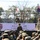 A multinational military ceremony titled 'Orient Shield 2026' is taking place at Hokkaido Training Area on September 17, 2026. Three flag bearers stand on an elevated stage holding the flags of the United States, Japan, and Australia, while military officers address assembled troops. The event appears to be an opening or closing ceremony for a joint military exercise involving at least three nations.