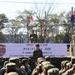 A multinational military ceremony titled 'Orient Shield 2026' is taking place at Hokkaido Training Area on September 17, 2026. Three flag bearers stand on an elevated stage holding the flags of the United States, Japan, and Australia, while military officers address assembled troops. The event appears to be an opening or closing ceremony for a joint military exercise involving at least three nations.