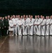 A large group photograph taken on what appears to be a stage or performance venue, featuring a mix of U.S. Navy personnel in white dress uniforms and civilians in formal attire. The group includes both men and women, with a notable presence of individuals of Asian descent among the civilian contingent on the left side. This appears to be a formal commemorative or diplomatic event involving military and civilian dignitaries.