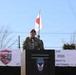 A U.S. Army officer wearing a red beret speaks at a podium bearing the 11th Airborne Division ('Arctic Airborne') insignia during an official military ceremony dated September 17, 2026. Three national flags — United States, Japan, and Australia — are displayed in the background, indicating a multinational military event. A banner partially visible behind the speaker references the same date in both English and Japanese.