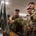 A group of military personnel in camouflage uniforms are gathered around a display screen or map board in what appears to be an indoor briefing or operations room. One soldier, wearing a distinctive green camouflage pattern consistent with Japanese Ground Self-Defense Force (JGSDF) uniform, is pointing at the display while others observe attentively. At least one soldier on the right wears a US Army MultiCam (OCP) uniform with a visible shoulder patch.