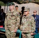 Two military personnel in MultiCam/OCP camouflage uniforms are standing at what appears to be an outdoor military ceremony or award presentation. The soldier on the right wears a U.S. Army uniform with a general officer rank insignia (one star visible on cap) and a name tape reading 'DEMONAY' or similar. The soldier on the left wears a green beret and has their face digitally obscured, with what appears to be a French flag patch on the sleeve.