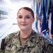 A U.S. Navy service member named Daugherty is photographed in a military corridor wearing the Navy Working Uniform (NWU) digital camouflage pattern. She is assigned to NMRTC Cherry Point, as indicated by the unit patch on her right sleeve. The setting appears to be an official military facility with a row of flags visible in the background.