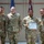BACH Conducts Commanders Monthly Awards Ceremony Four U.S. Army soldiers in OCP (Operational Camouflage Pattern) uniforms pose for a photo during a military awards ceremony. One female soldier holds a 'Commander's Certificate of Achievement' and appears to be wearing a medal, indicating she is the recipient of the award. The group is standing in front of American and unit flags in what appears to be a military facility.
