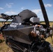 The image shows a light-sport aircraft or powered parachute/paramotor buggy with a carbon fiber body, registration number N184SR, parked on an open grassy field. The vehicle features a rear-mounted pusher propeller, a visible engine with turbocharger components, and an intercooler, with what appears to be a parachute or canopy stored in a black bag on top. The setting is a rural airstrip or open field under partly cloudy skies.