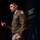 LT. Gen. Stanton Speaks at DAFITC A U.S. Army officer in dress uniform is speaking at a conference or event identified as 'DAFITC 2026' visible on the backdrop. The officer is gesturing with a raised fist while delivering a presentation on stage. Multiple military insignia, patches, and medals are visible on the uniform.