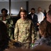 A U.S. Army soldier identified by name tape as 'STANTON' is engaged in conversation with a group of civilians in what appears to be an indoor meeting or conference setting. The soldier is wearing OCP (Operational Camouflage Pattern) uniform with 'U.S. ARMY' tape visible and rank insignia on the chest. The gathering appears to be a professional or community engagement event with a diverse group of attendees.