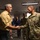 Lt. Gen. Stanton visits DISA Montgomery. A civilian man in a yellow shirt is shaking hands with a U.S. Army soldier in OCP (Operational Camouflage Pattern) uniform. The meeting appears to be taking place in an office or government building environment. Several other individuals are visible in the background observing the exchange.