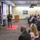 Lt. Gen. Stanton speaks at DISA annual awards ceremony. A military officer in Army dress uniform is delivering a speech or presentation at a formal event, standing on a red carpet in front of a seated audience. The setting appears to be an official government or defense agency conference room, identifiable by the 'Defense Information Systems Agency' (DISA) branded table covering and multiple military flags. A projection screen displays a slide behind a wooden podium.
