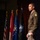 Lt. Gen. Stanton speaks at DAFITC A U.S. Army officer in dress uniform stands on a stage, appearing to deliver a speech or presentation. He is wearing an olive green Army Service Uniform with visible rank insignia, a Ranger tab, a shoulder patch, and service ribbons. Multiple flags are displayed in the background, including the U.S. flag and what appear to be military branch and unit flags.