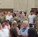 A group of U.S. Army soldiers in OCP (Operational Camouflage Pattern) uniforms are standing at attention or in formation during what appears to be a military ceremony or event. They are surrounded by seated civilian attendees, likely family members and guests, in what looks like an indoor venue or gymnasium. The event appears to be a formal military occasion such as a graduation, promotion ceremony, or unit activation.