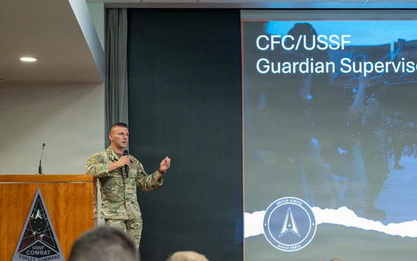 A military officer in camouflage uniform is presenting at a podium bearing the USSF Combat Forces Command emblem to an audience of uniformed personnel. The presentation slide behind him reads 'CFC/USSF Guardian Supervisor Course' and displays the United States Space Force logo. The setting appears to be a formal briefing room or auditorium.