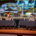 Four U.S. Army soldiers in combat uniforms are seated at a panel discussion table on a stage. The projected screen behind them identifies participants including CSM Alejandro Fundo, COL Nick Sinclair, CSM Ryan Dilling from the 3rd SBCT, 4th Infantry Division 'Arrowhead,' and a moderator COL Cannon commanding the 16th CAV Brigade. The event appears to be a formal military symposium or leadership forum.
