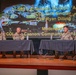 Four U.S. Army soldiers in combat uniforms are seated at a panel table on a stage, participating in a military briefing or discussion event. The projected screen behind them identifies the event as involving the 3rd SBCT, 4th Infantry Division 'Arrowhead,' with named participants COL Nick Sinclair, CSM Ryan Dilling, and moderator COL Cannon, Commander 16th CAV Brigade. The setting appears to be an auditorium or theater-style venue.