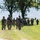 Georgia ANG Leadership Symposium 2026 A column of military personnel in full combat gear marches along a dirt path through an open grassy field. The soldiers are equipped with rifles, tactical vests, helmets, and backpacks, suggesting a field training exercise or patrol movement. The formation stretches back into the distance with approximately 15-20 visible personnel.