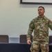 A U.S. Army Colonel named Wright, wearing Operational Camouflage Pattern (OCP) uniform, is speaking or briefing in what appears to be a conference or classroom setting. He is gesturing with his right hand, suggesting he is actively addressing an audience. At least one other uniformed individual is partially visible in the foreground to the right.