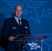 A uniformed U.S. Air Force or Space Force officer is speaking at a podium during an Air &amp; Space Forces Association (AFA) event. The officer is wearing a dark blue service dress uniform with multiple ribbons and decorations. The backdrop prominently displays the AFA logo repeated across a blue-toned background.