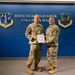 Two military personnel in OCP (Operational Camouflage Pattern) uniforms pose together holding a certificate or official document at Hancock Field Air National Guard Base, home of the 174th Attack Wing. The setting appears to be an official ceremony, likely a promotion or award presentation. The backdrop features the Air National Guard and 174th Attack Wing insignia on a blue wall.