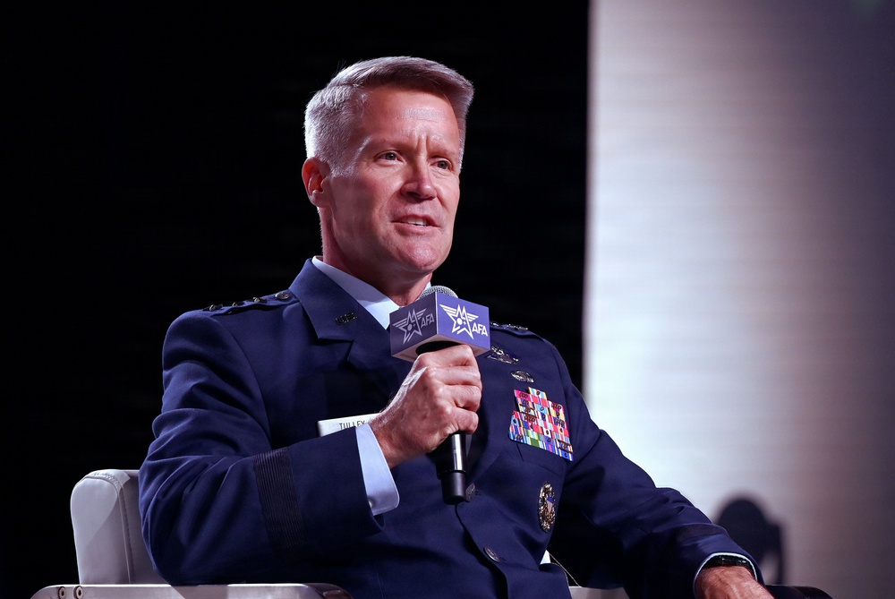 A senior U.S. Air Force officer in dress blue uniform is seated and speaking into an AFA (Air Force Association) branded microphone at what appears to be a formal military conference or symposium. The officer displays numerous service ribbons and medals on their uniform, indicating extensive military service. The event appears to be an AFA-sponsored panel discussion or interview session.