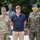 Department of War Delegation visits Poland Three men pose for a photo in front of a bronze bust monument in an outdoor setting. Two of the men are in military uniforms — one wearing a U.S. Army uniform with the name tape 'MOUNTFORD' and a brigadier general star insignia, and the other wearing a Polish Army uniform with a green beret and Polish flag patch. The civilian in the center is dressed in a navy polo shirt and khaki trousers.
