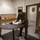 Department of War Delegation visits Poland Three military personnel are gathered around a round table in what appears to be a military office or reception area. A soldier in a distinctive camouflage pattern — consistent with Polish Armed Forces uniform — is signing a guest book or official document, while two U.S. Army soldiers in MultiCam/OCP uniforms observe. The setting includes military insignia, unit patches, and a poster on the wall suggesting a U.S. Army unit headquarters.