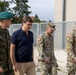 The image shows a group of four individuals walking together in what appears to be a military installation or base. The group includes one Polish military officer in camouflage uniform with a green beret, one civilian in a navy polo shirt, and two U.S. Army soldiers in MultiCam (OCP) uniforms. The setting suggests an official visit or coordination meeting between allied military and civilian personnel.