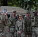 A group of four U.S. Army soldiers in MultiCam (OCP) camouflage uniforms pose for a photo in front of a tan military HMMWV (Humvee). A fifth soldier, with the name tape 'RAINES' visible, photographs them using a smartphone. One of the posing soldiers has the name tape 'WEIMER' visible, and the setting appears to be an urban environment.