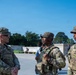 Three U.S. Army soldiers in Operational Camouflage Pattern (OCP) uniforms are engaged in conversation outdoors in what appears to be a public or ceremonial area. The soldier on the left is smiling and wearing name tapes and a 3rd Infantry Division patch. The setting appears to be a well-maintained outdoor plaza or memorial area with trees and clear blue sky in the background.