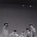 A black-and-white archival photograph, appearing to be a film negative or slide, depicting a group of military personnel in uniform on what appears to be a raised platform or stage. Several individuals are in saluting positions, suggesting a formal military ceremony or official event. The image shows characteristics of mid-20th century military photography.