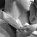A black and white close-up photograph showing a person fastening or adjusting a cufflink on a dress shirt sleeve. A second person's hand is visible performing the action, suggesting assistance being given, possibly in a formal dressing context. The image has an intimate, candid quality consistent with event or wedding photography.