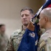 Two U.S. Army soldiers in OCP (Operational Camouflage Pattern) uniforms are participating in a military ceremony, likely a change of command or activation/inactivation ceremony. The soldier identified by his name tape as 'METZLER' is holding a blue unit guidon/colors with gold fringe, featuring an eagle emblem and partial text reading 'INFANTRY'. A second soldier is assisting in handling the flag.