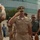 C3F conducts Chief pinning ceremony A group of U.S. Navy personnel in Service Khaki (Type B) uniforms are engaged in a formal saluting ceremony outdoors. The central figure, a senior officer with command insignia and multiple service ribbons, is returning a salute from subordinates. The setting appears to be a military installation or official venue with a modern curved glass building in the background.